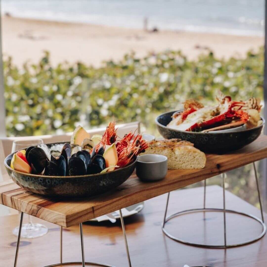 A wooden platter filled with two bowls of prawns and seafood
